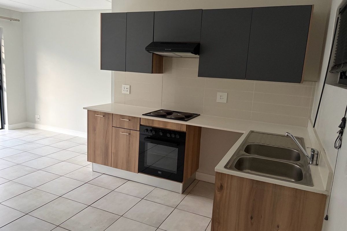 Modern kitchen featuring two-tone cabinetry, built-in oven and hob, extractor fan, and double stainless steel sink with tiled flooring.