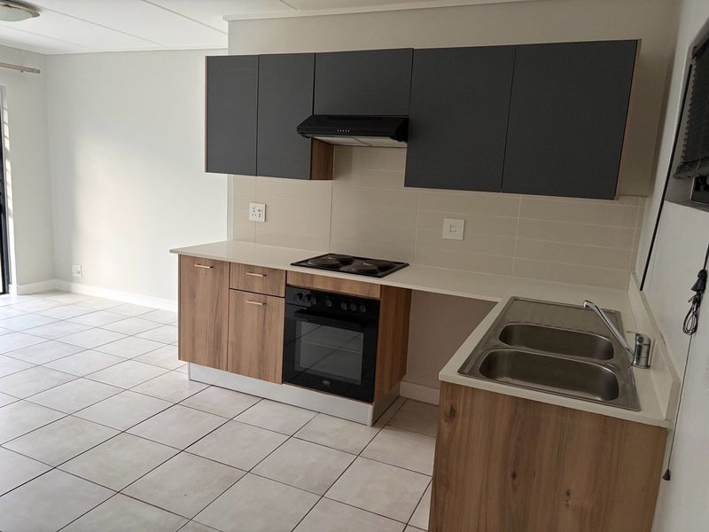 Modern kitchen featuring two-tone cabinetry, built-in oven and hob, extractor fan, and double stainless steel sink with tiled flooring.