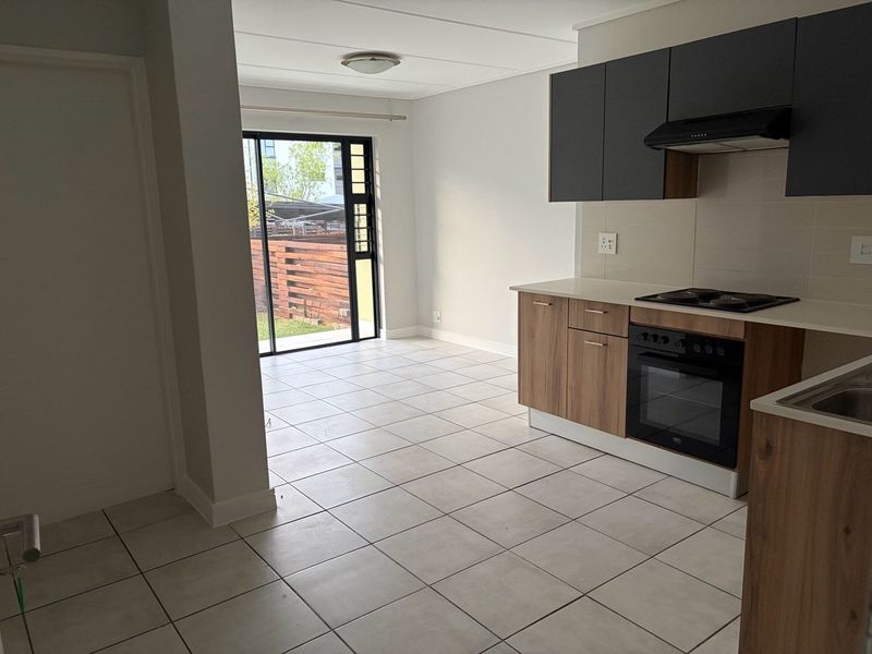 Open-plan kitchen and living area featuring modern cabinetry, built-in appliances, tiled flooring, and direct access to an outdoor space through a sliding glass door.
