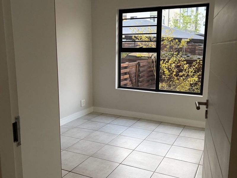 A bright, empty bedroom featuring neutral tiled flooring, a modern black-framed window, and a simple pendant light fixture.