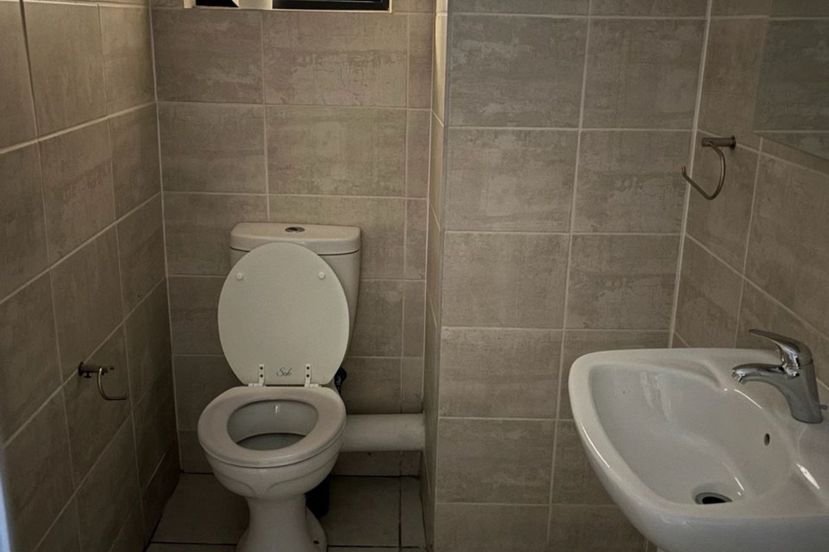 A compact bathroom featuring neutral wall and floor tiles, a pedestal basin with a mixer tap, and a standard toilet.