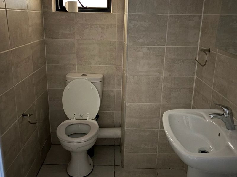 A compact bathroom featuring neutral wall and floor tiles, a pedestal basin with a mixer tap, and a standard toilet.