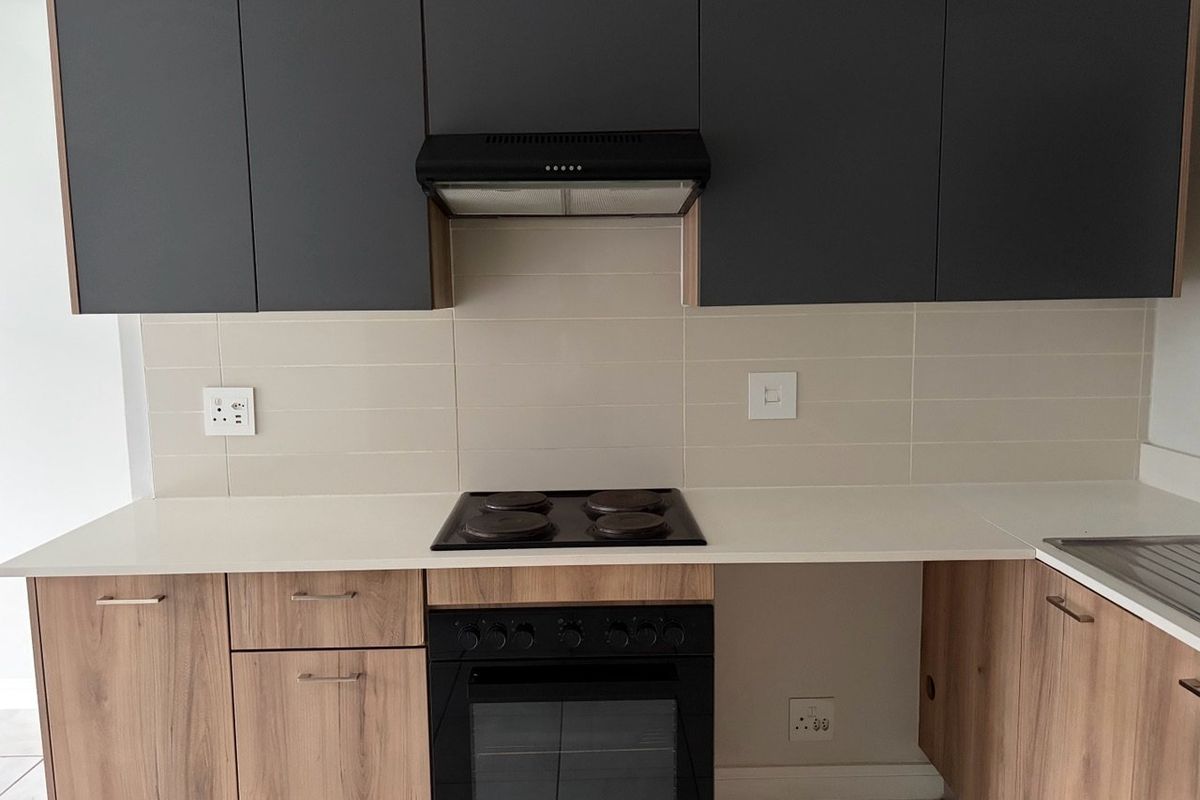 Modern kitchen featuring dark grey upper cabinets, wood-finish lower cabinetry, white stone countertops, and integrated electric hob and oven.