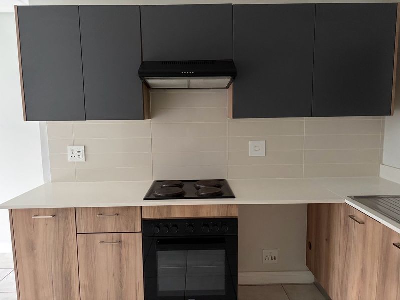 Modern kitchen featuring dark grey upper cabinets, wood-finish lower cabinetry, white stone countertops, and integrated electric hob and oven.