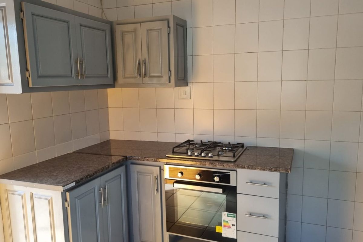 A functional kitchen area featuring grey built-in cabinetry, a gas hob, a built-in oven, and tiled splashback walls.