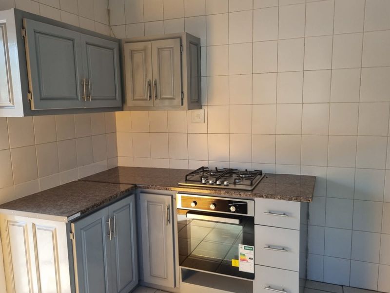 A functional kitchen area featuring grey built-in cabinetry, a gas hob, a built-in oven, and tiled splashback walls.
