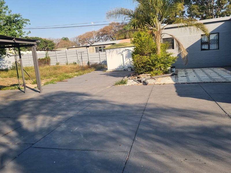 Rear exterior area featuring a large paved driveway, a metal pergola, a small storage shed, and a precast concrete boundary wall.
