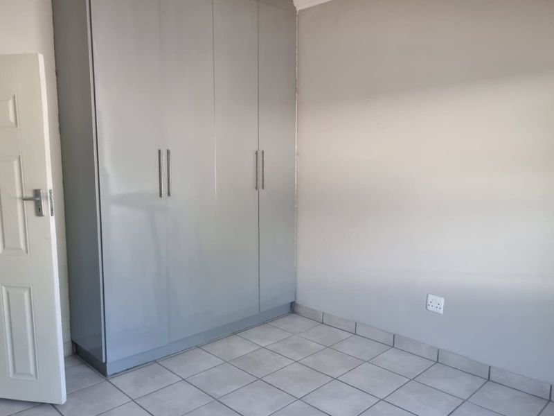 A clean, empty bedroom featuring neutral grey walls, light-colored floor tiles, and a modern built-in wardrobe with sleek handles.
