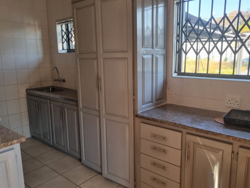 A functional kitchen featuring built-in cabinetry, laminate countertops, a stainless steel sink, and tiled flooring with security bars on the windows.
