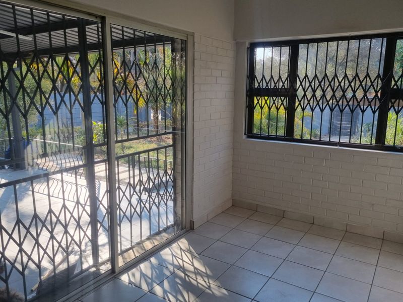 A bright, empty sunroom or enclosed patio featuring tiled floors, painted brick walls, and secure sliding glass doors leading to the garden.
