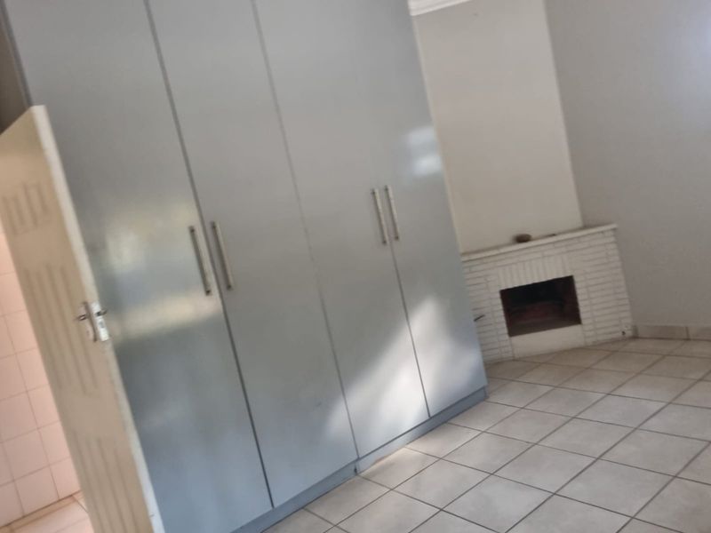 A bedroom featuring built-in cupboards, a brick fireplace, and tiled flooring.