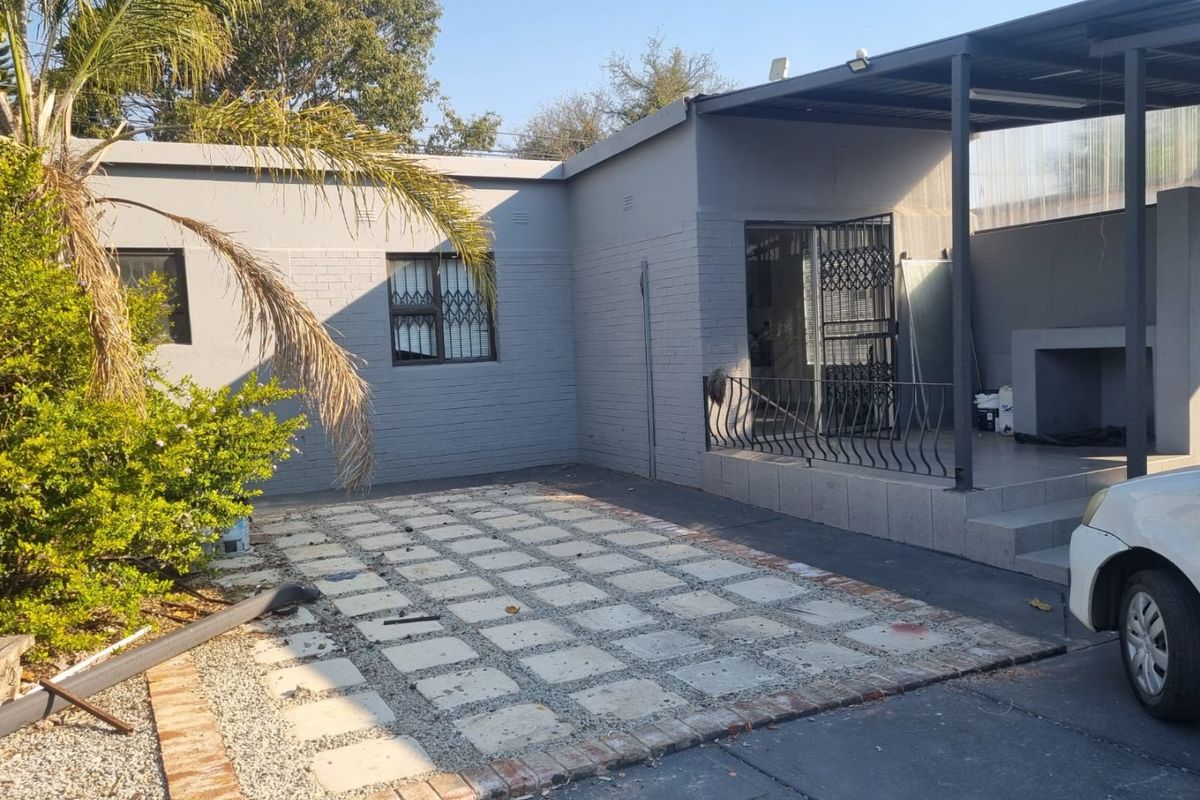 Rear exterior view featuring a covered patio with a built-in braai, paved area, and secure access to the main dwelling.