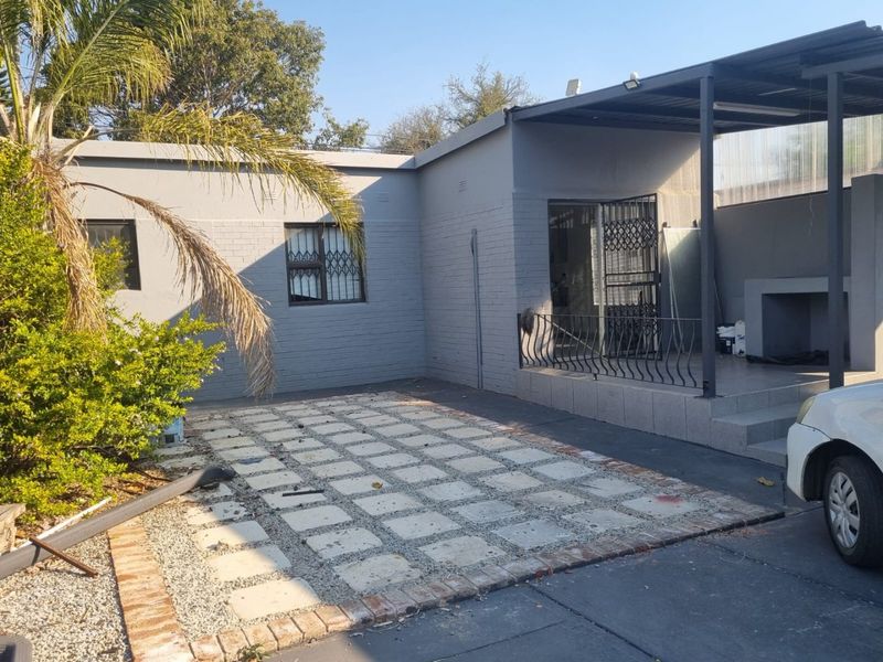 Rear exterior view featuring a covered patio with a built-in braai, paved area, and secure access to the main dwelling.