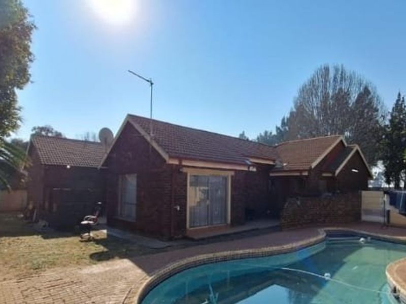 Rear exterior view of the house featuring a swimming pool, brick paved patio area, and established garden surroundings.