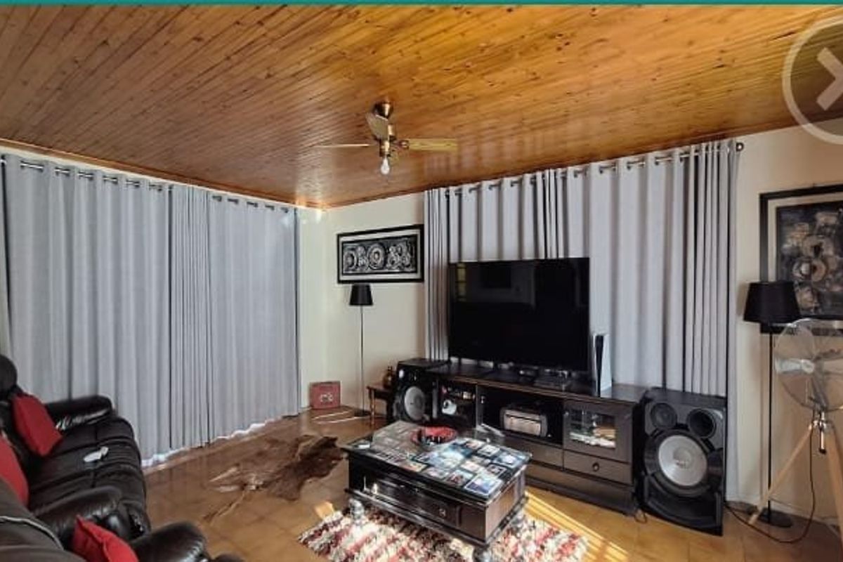 A living room featuring a distinctive timber-clad ceiling, ceiling fan, and tiled flooring, providing a warm and functional space for relaxation.