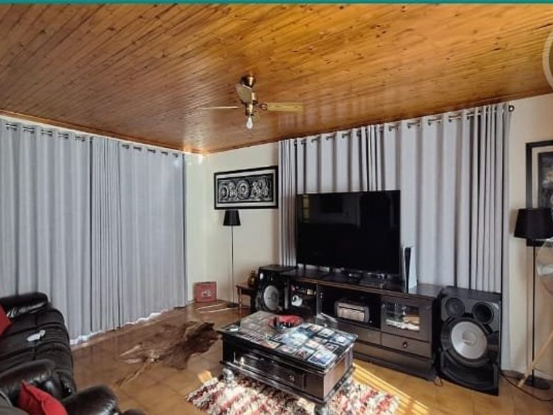 A living room featuring a distinctive timber-clad ceiling, ceiling fan, and tiled flooring, providing a warm and functional space for relaxation.