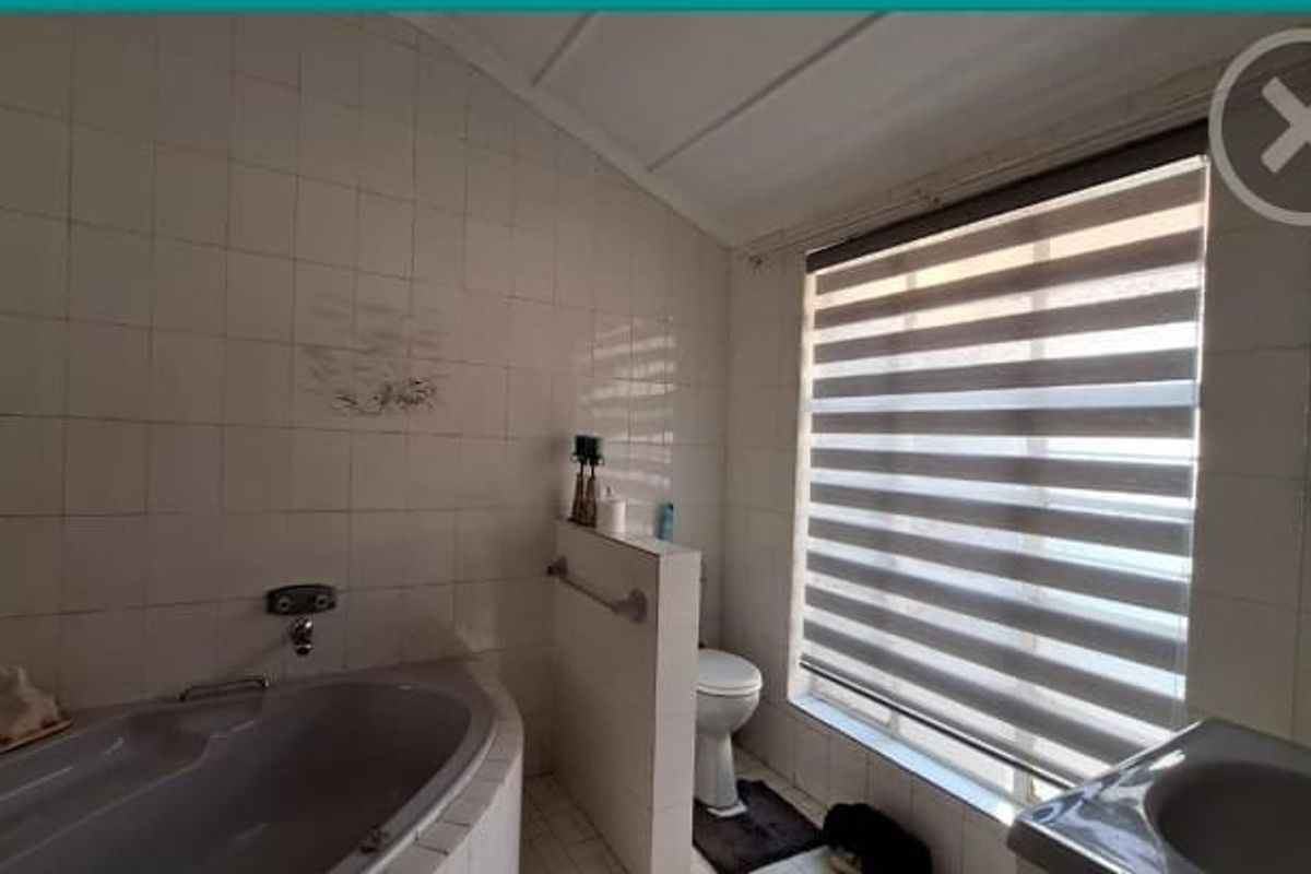 A functional bathroom featuring a built-in bathtub, toilet, and vanity basin with tiled walls and flooring, offering potential for modern renovation.
