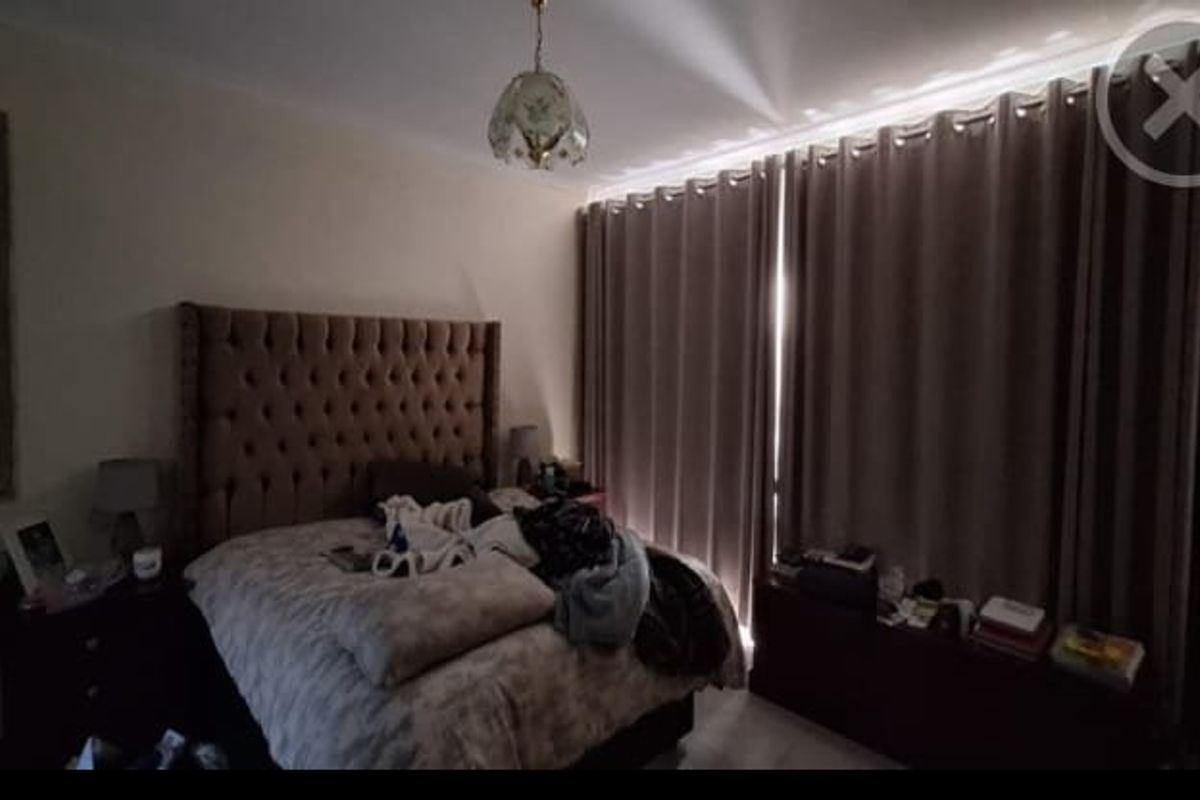 A bedroom featuring a neutral color palette, large window with full-length curtains, and a central ceiling light fixture.