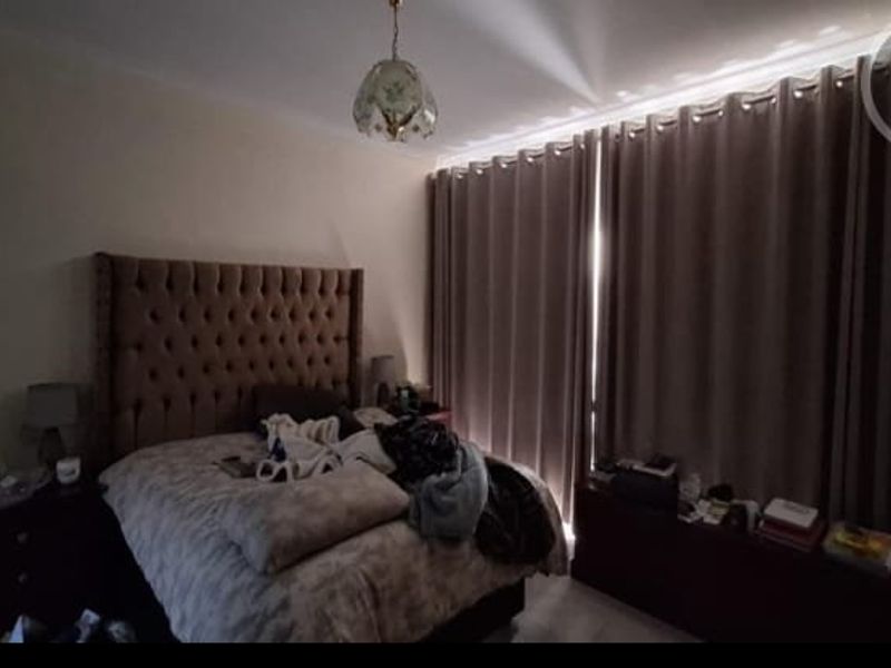 A bedroom featuring a neutral color palette, large window with full-length curtains, and a central ceiling light fixture.