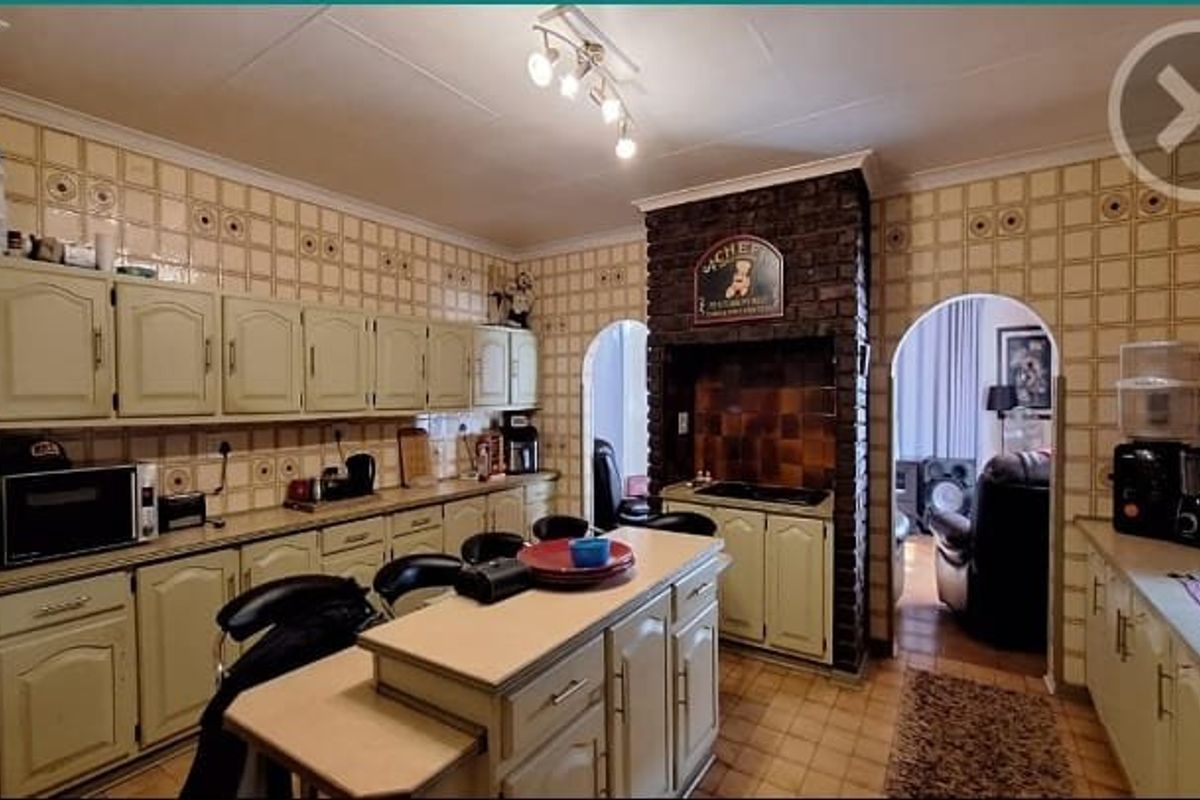 A dated kitchen featuring extensive wall tiling, built-in cabinetry, a central island, and a distinctive brick feature wall with an arched entryway.