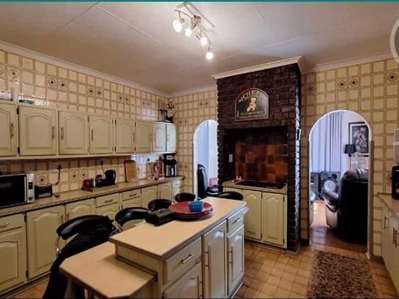 A dated kitchen featuring extensive wall tiling, built-in cabinetry, a central island, and a distinctive brick feature wall with an arched entryway.