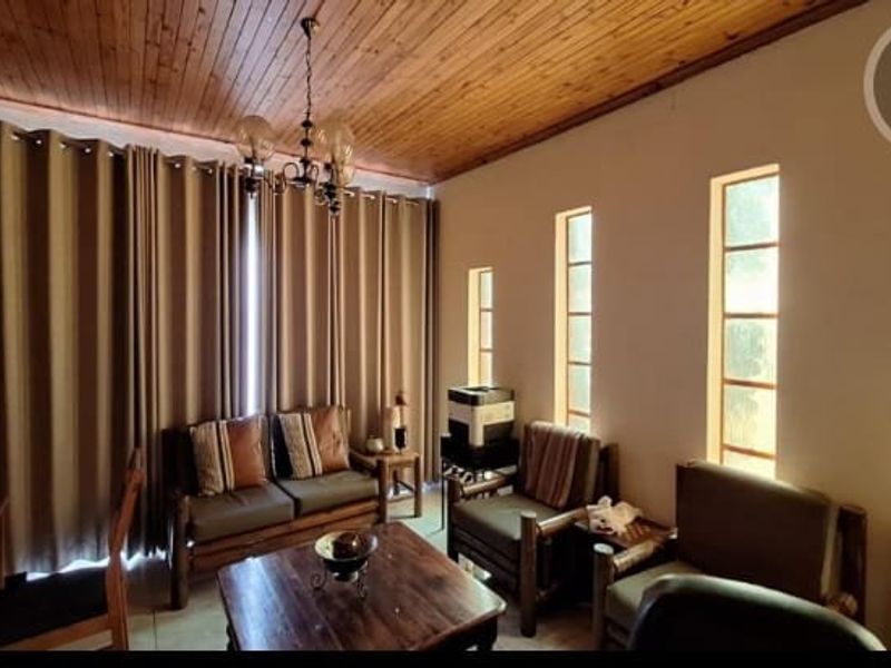 A living room featuring a timber-clad ceiling, a central chandelier, and multiple vertical windows providing natural light.