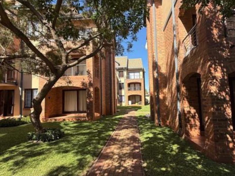 A well-maintained apartment complex exterior featuring red brick facades, private balconies, and a landscaped garden with a paved walkway.
