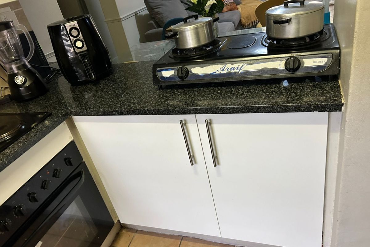 A functional kitchen area featuring granite countertops, built-in oven, and white base cabinetry with tiled flooring.