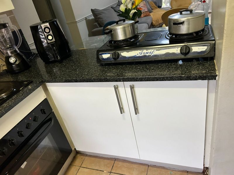 A functional kitchen area featuring granite countertops, built-in oven, and white base cabinetry with tiled flooring.