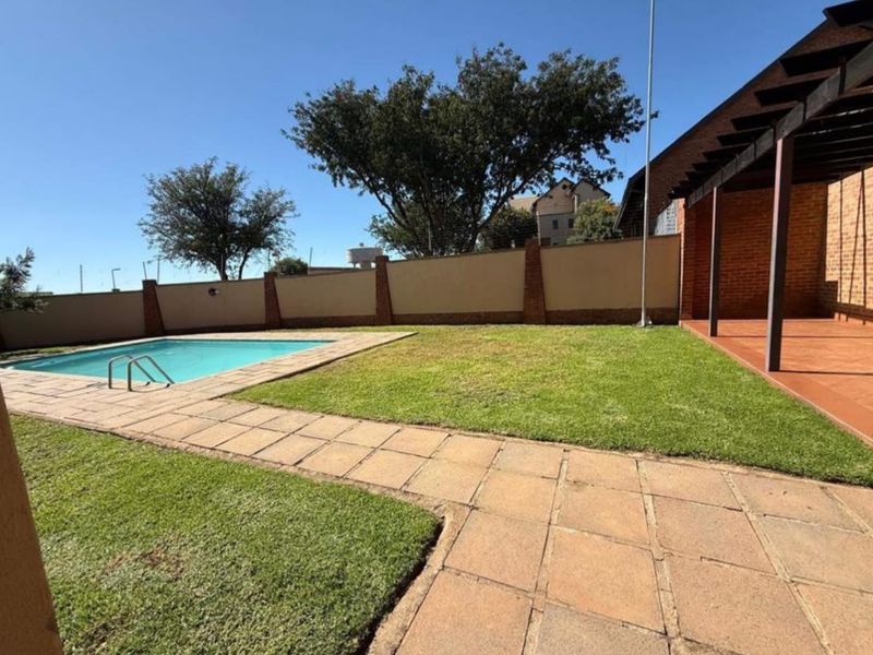 A private outdoor area featuring a swimming pool, paved patio, lawn, and a covered pergola structure.