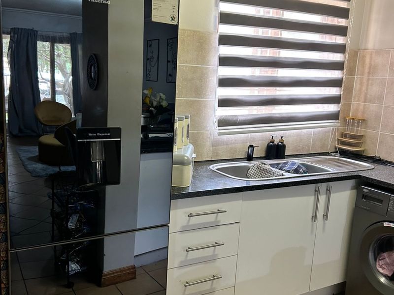 A functional kitchen area featuring white cabinetry, a stainless steel sink, tiled backsplash, and space for a washing machine under the counter.