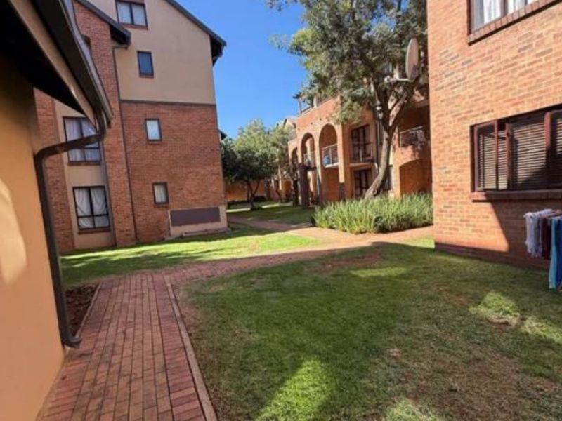 A view of the communal garden area between apartment blocks, featuring brick pathways, well-maintained lawns, and established trees.