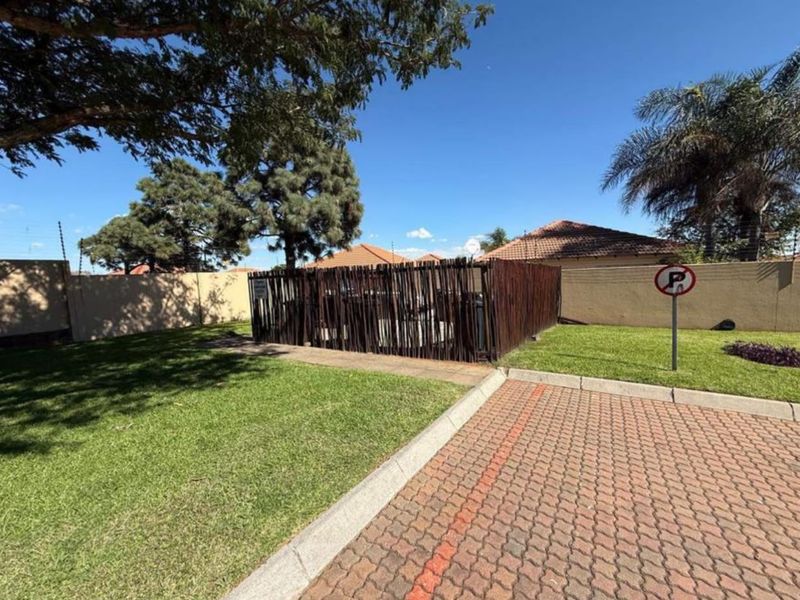 Exterior view of the apartment complex grounds featuring a paved driveway, manicured lawn, and perimeter wall with electric fencing.
