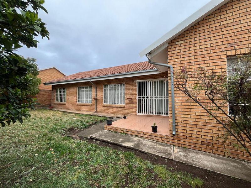 Rear view of the apartment featuring a face brick facade, tiled patio area, security gates, and a surrounding garden space.