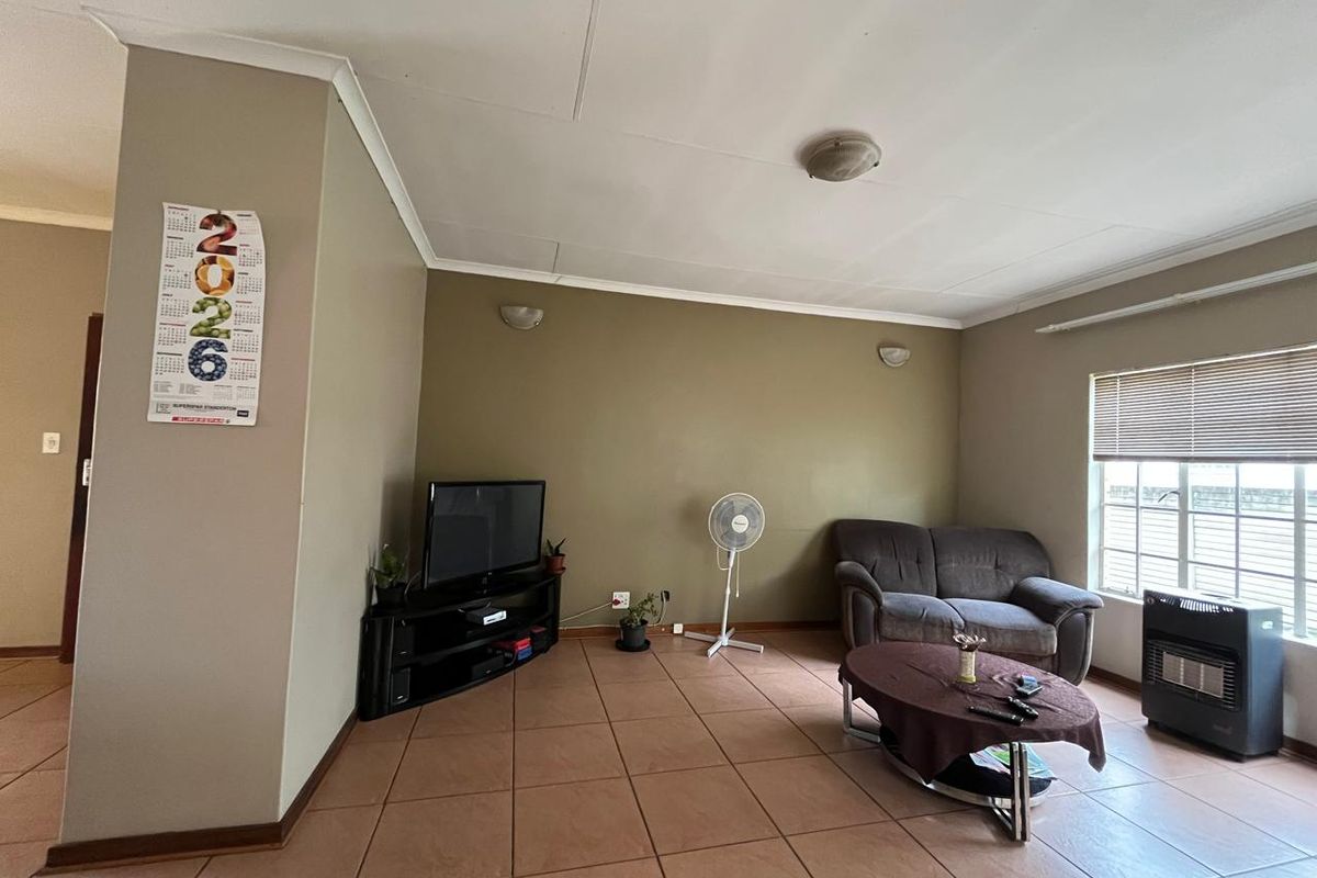 A living room featuring tiled flooring, wall-mounted lighting, and a built-in gas heater, offering a functional space with potential for cosmetic updates.