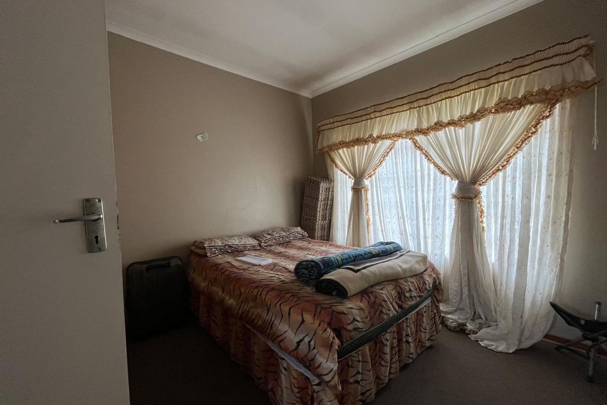 A standard bedroom featuring carpeted flooring, neutral wall finishes, and a large window dressed with traditional curtains.