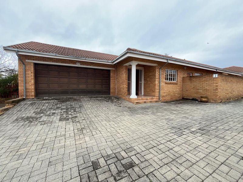 Front exterior view of a brick apartment unit featuring a paved driveway, double garage, and a covered entrance with a security gate.