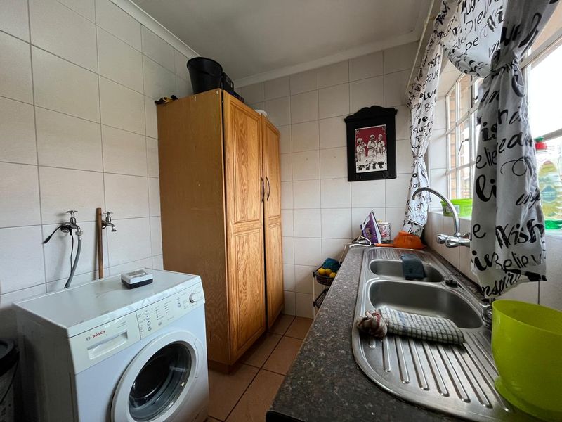 A functional laundry room featuring tiled walls, a double stainless steel sink, and dedicated plumbing connections for a washing machine.