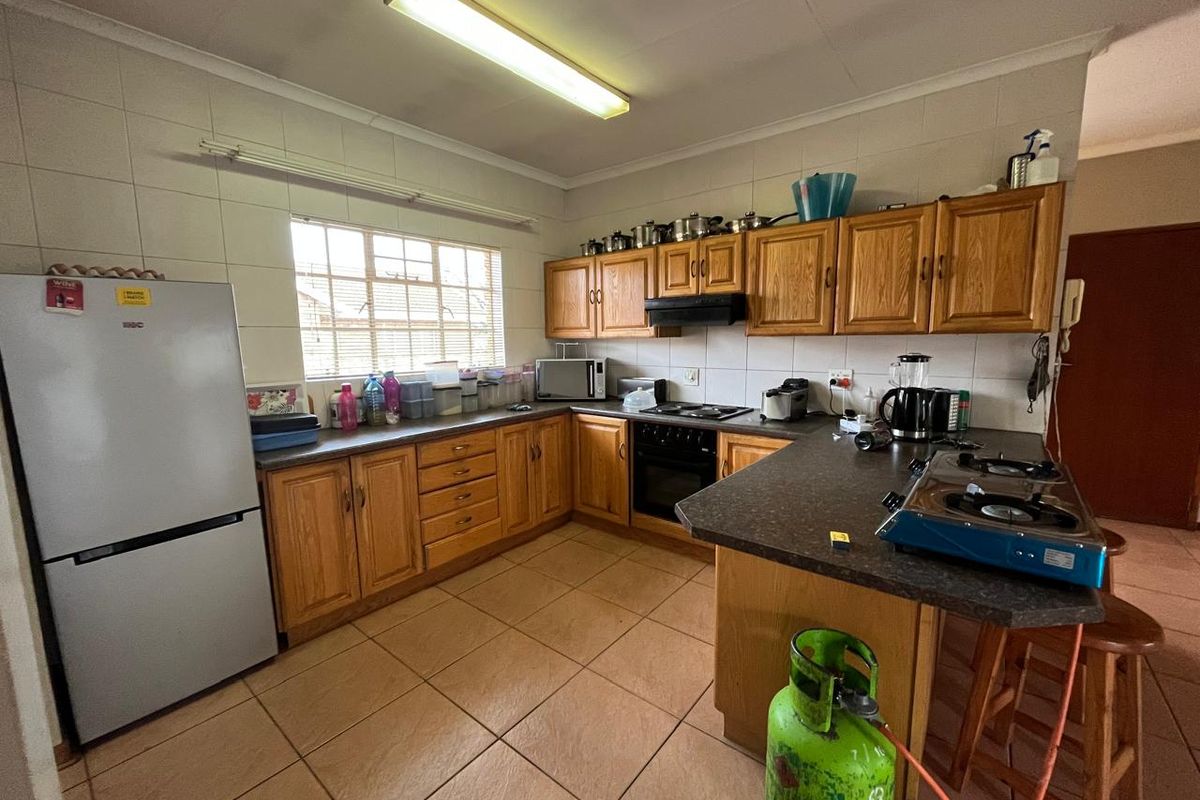A functional kitchen featuring wooden cabinetry, laminate countertops, a built-in oven with hob, and tiled flooring throughout.