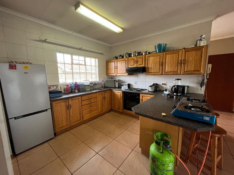 A functional kitchen featuring wooden cabinetry, laminate countertops, a built-in oven with hob, and tiled flooring throughout.
