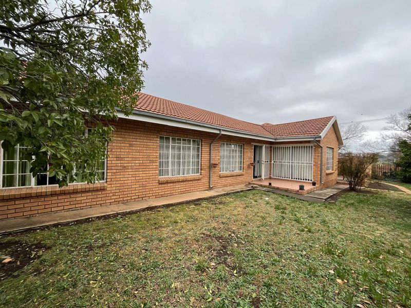 Rear view of a face brick apartment building featuring a tiled roof, security bars on windows, and a paved patio area overlooking the lawn.