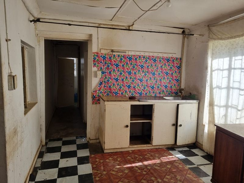 A dilapidated kitchen space featuring basic cabinetry, a stainless steel sink, and worn flooring, requiring significant renovation and repair to restore functionality.