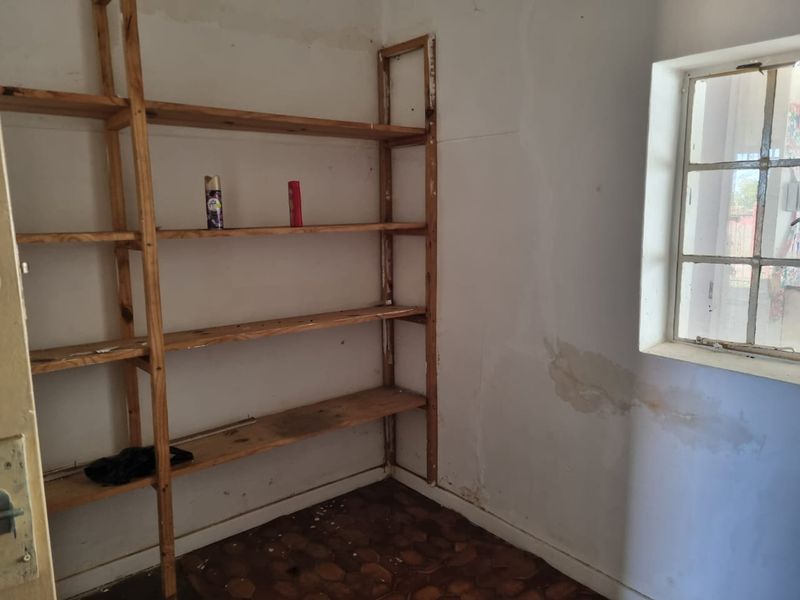 A small utility or storage room featuring built-in wooden shelving, a steel-framed window, and visible signs of wall moisture and wear.