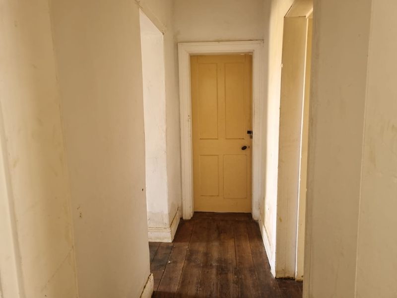 A narrow hallway featuring original timber flooring, painted walls, and a classic internal door, requiring cosmetic updates to refresh the space.