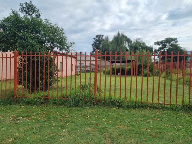 A view of the rear garden featuring a lawn area enclosed by red metal spike fencing and a small covered outdoor structure.