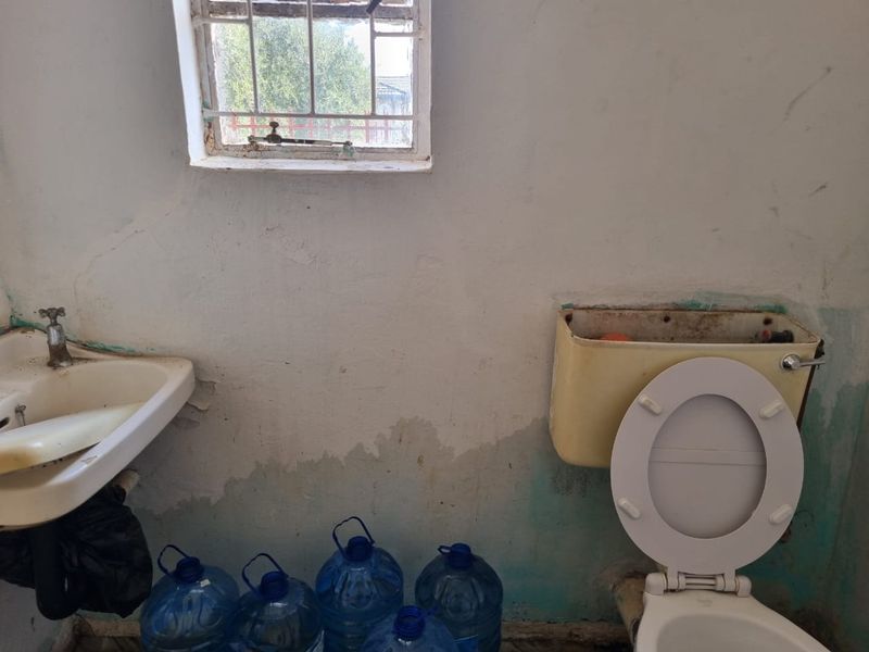 A bathroom in need of significant renovation, featuring a wall-mounted basin and toilet with visible signs of wall damage and surface deterioration.