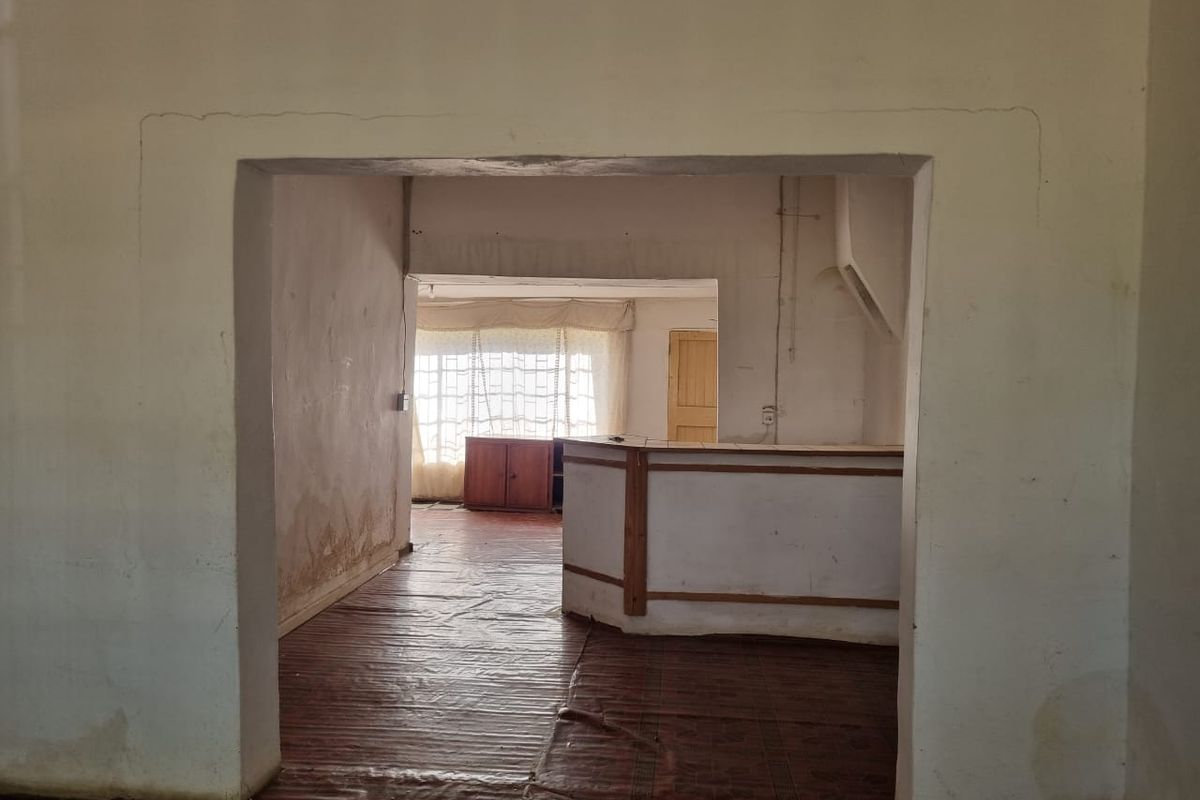 An empty living area featuring a built-in bar counter, tiled flooring, and an archway, requiring significant cosmetic renovation and wall repairs.