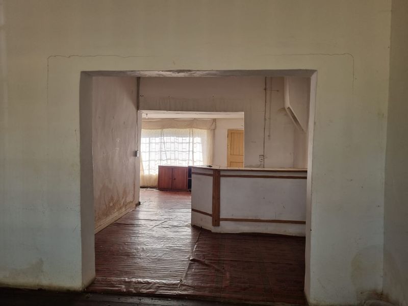 An empty living area featuring a built-in bar counter, tiled flooring, and an archway, requiring significant cosmetic renovation and wall repairs.