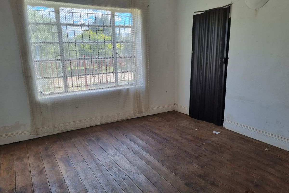 An empty bedroom featuring original timber flooring, a large window with security bars, and a folding door, requiring cosmetic updates.