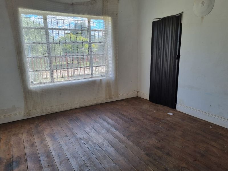 An empty bedroom featuring original timber flooring, a large window with security bars, and a folding door, requiring cosmetic updates.